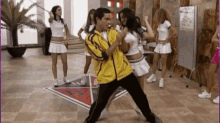a man in a yellow jacket is dancing in front of a group of cheerleaders