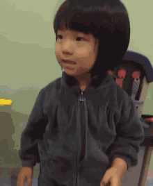 a little girl wearing a grey jacket is standing in front of a stroller