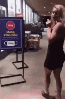 a woman is standing in front of a sign that says mask required