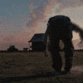 a man walking in a dirt field with a house and truck in the background
