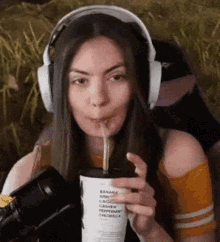 a woman wearing headphones is drinking from a cup with a straw ..