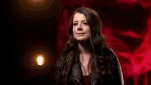 a woman in a black leather jacket is standing in front of a red wall .