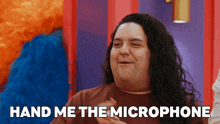 a man with long hair and a nose ring is asking for a hand me the microphone