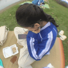 a girl in a blue jacket is sitting on a mat eating a snack