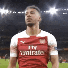 a soccer player wearing a red fly emirates jersey is standing on a soccer field .
