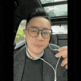 a man wearing glasses and ear buds is sitting in the back seat of a car