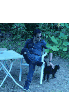 a man sits in a chair with his legs crossed next to a black cat
