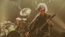 a man sings into a microphone while playing a guitar in front of a drum set with the letter d on it
