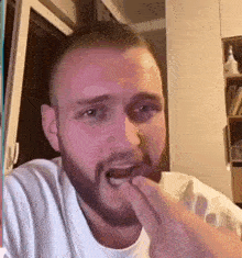 a man with a beard and a white shirt is eating something with his hands .