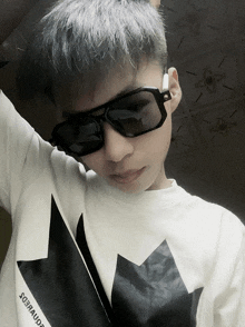 a boy wearing sunglasses and a white shirt with a black maple on it