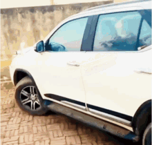 a white suv is parked on a brick driveway next to a wall
