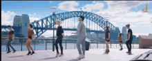 a group of people are dancing in front of a bridge that says sydney on it