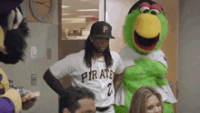 a man in a pirates jersey is standing next to a green mascot .