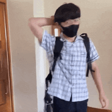 a man wearing a mask and a plaid shirt is standing in a room .