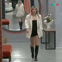 a woman walking down a hallway with a vase of flowers on a table