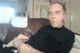 a man in a black shirt sits on a couch with his eyes closed
