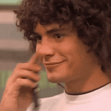 a young man with curly hair is talking on a cell phone and smiling .