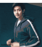 a man wearing a blue hoodie with white stripes on the sleeves is standing in front of a blue wall ..