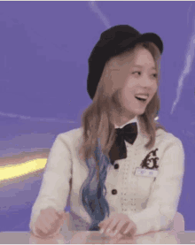 a girl wearing a black hat and a white sweater is sitting at a table and smiling .