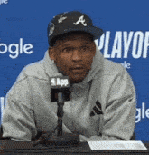 a man wearing a hat with the letter a on it sits in front of a microphone