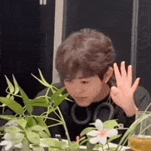 a young man is sitting at a table with flowers and giving a thumbs up sign .