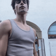 a man wearing a grey tank top is standing in front of a white building .