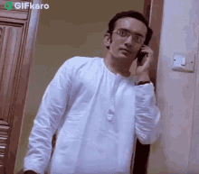 a man wearing glasses is talking on a cell phone while standing next to a door .