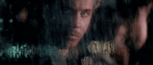 a close up of a man 's face behind a window with rain drops on it .