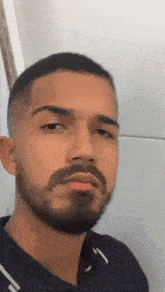 a man with a beard is making a funny face while standing in front of a white wall .