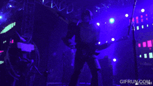 a man playing a guitar on a stage with purple lights and a gifrun.com logo