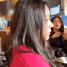a woman in a pink sweater looks over her shoulder at another woman