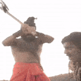 a shirtless man with a beard and mustache is holding a sword in his hands .