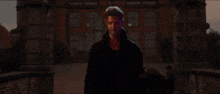 a man in a black coat stands in front of a red building