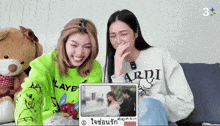 a woman wearing a white ardi sweatshirt sits next to another woman wearing a green sweatshirt