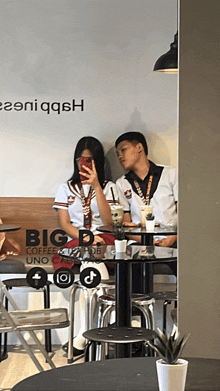two people sitting at a table in front of a sign that says big d coffee