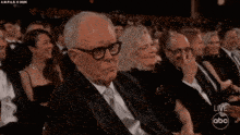an older man in a suit and tie is sitting in a crowd watching a live abc show