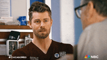 a man in a chicago medical center scrub shirt talks to another man
