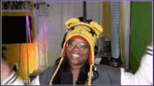 a woman wearing a yellow hat with ears and glasses is smiling in a room .
