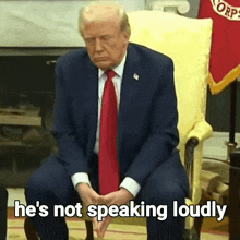 a man in a suit and tie is sitting in a chair with the words he 's not speaking loudly below him