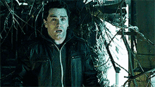 a man in a black jacket is standing in front of a broken window