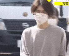 a man wearing a face mask and glasses is standing in front of a car .