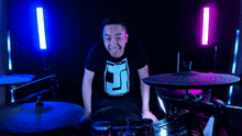a man in a black shirt with the letter j on it is sitting in front of a drum set