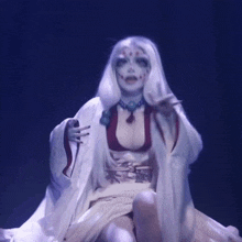 a woman with white hair and face paint is dancing on a blue background