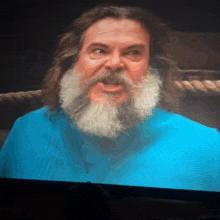 a man with long hair and a beard wearing a blue shirt looks at the camera