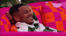 a man is laying on a pink couch with a checkered blanket .