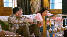 a man and a woman are sitting on a couch with the nbc destination x written on the bottom