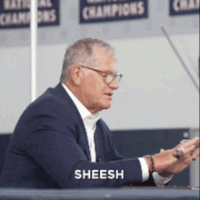 a man in a suit is sitting at a table and the word sheesh is on his arm
