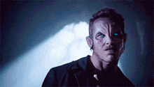 a man with blue eyes is standing in a dark room looking at the camera .