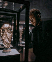a man wearing glasses looks at a gold trophy in a glass case
