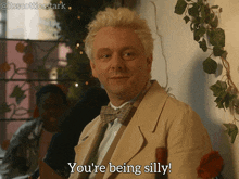 a man in a tan suit and bow tie says you 're being silly